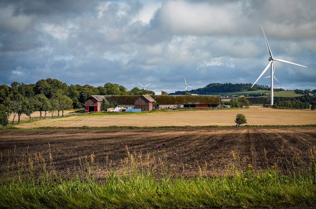 Vindkraftverk över åkrar och gårdar på den svenska landsbygden